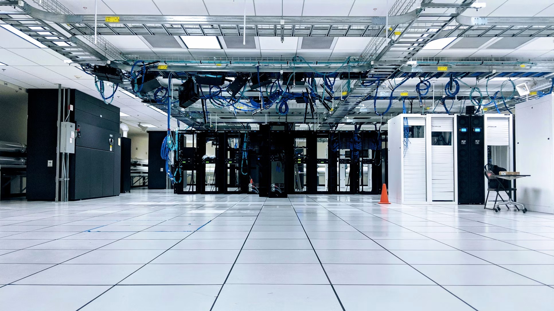 Rows of server cabinets beneath overhead network cables in a data center.